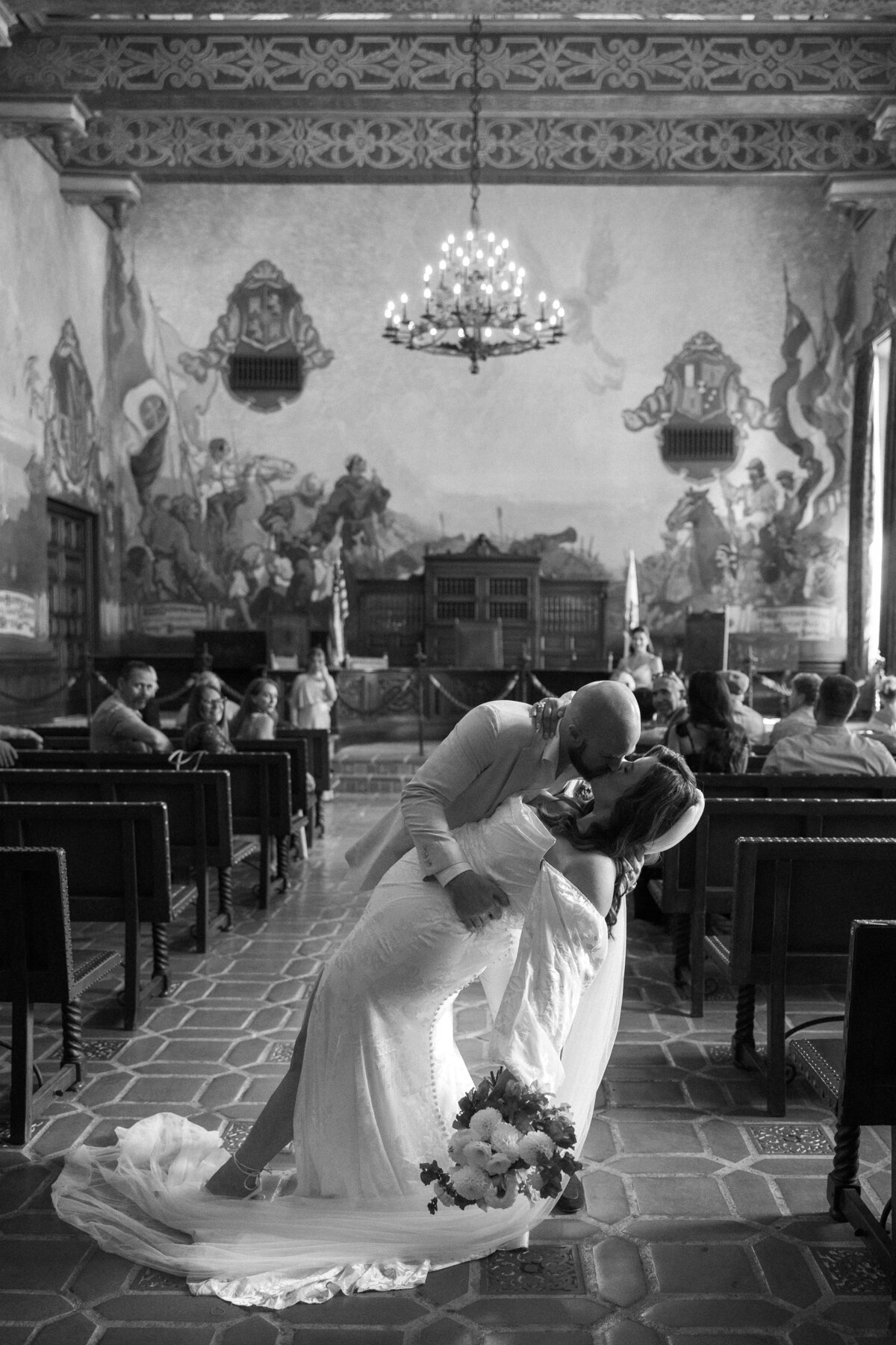 black and white photo of bride and grooms first kiss in the mural room at the Santa barbara courthouse