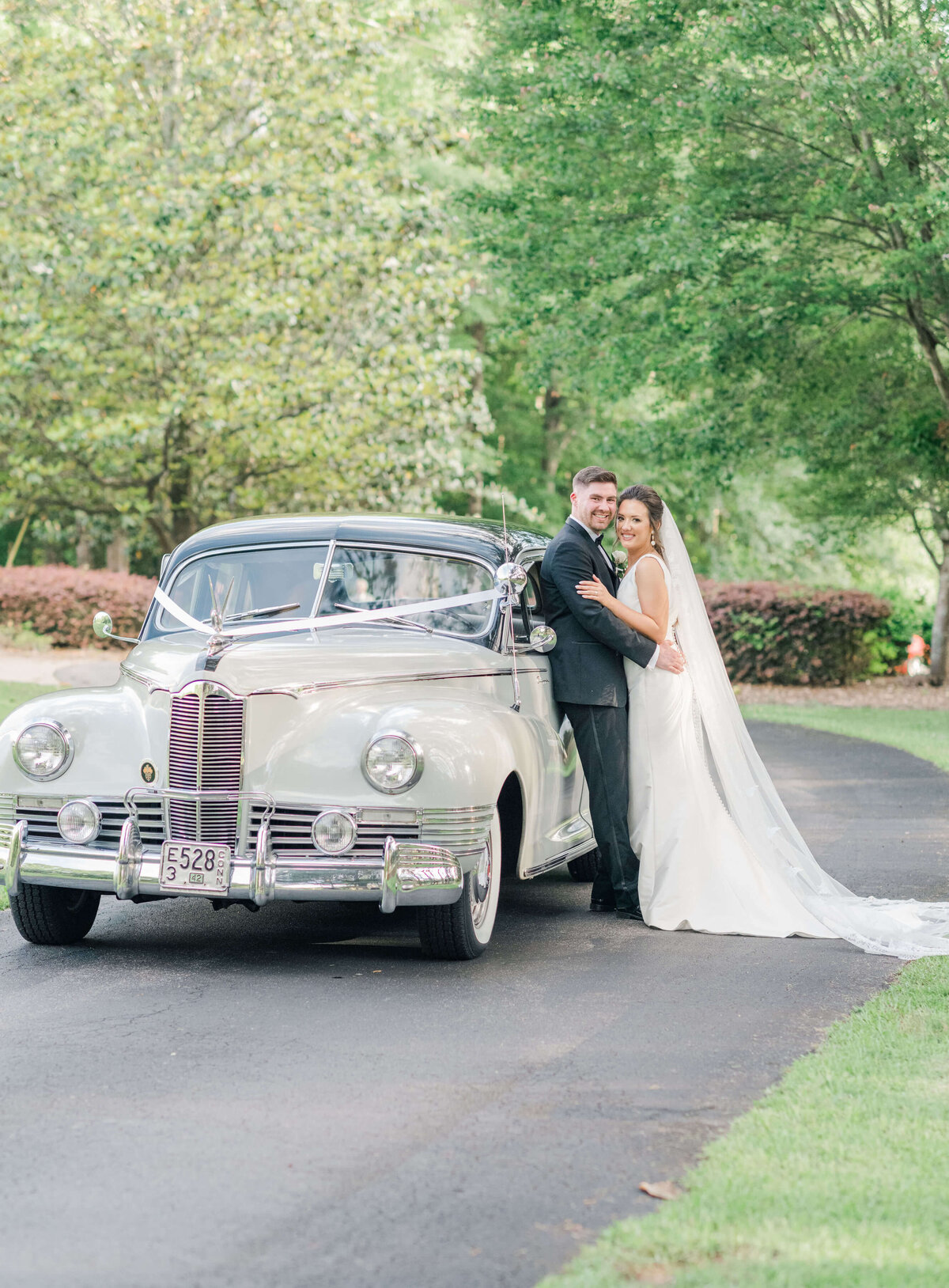 Bride and groom leaning against classic car for bridal portraits
