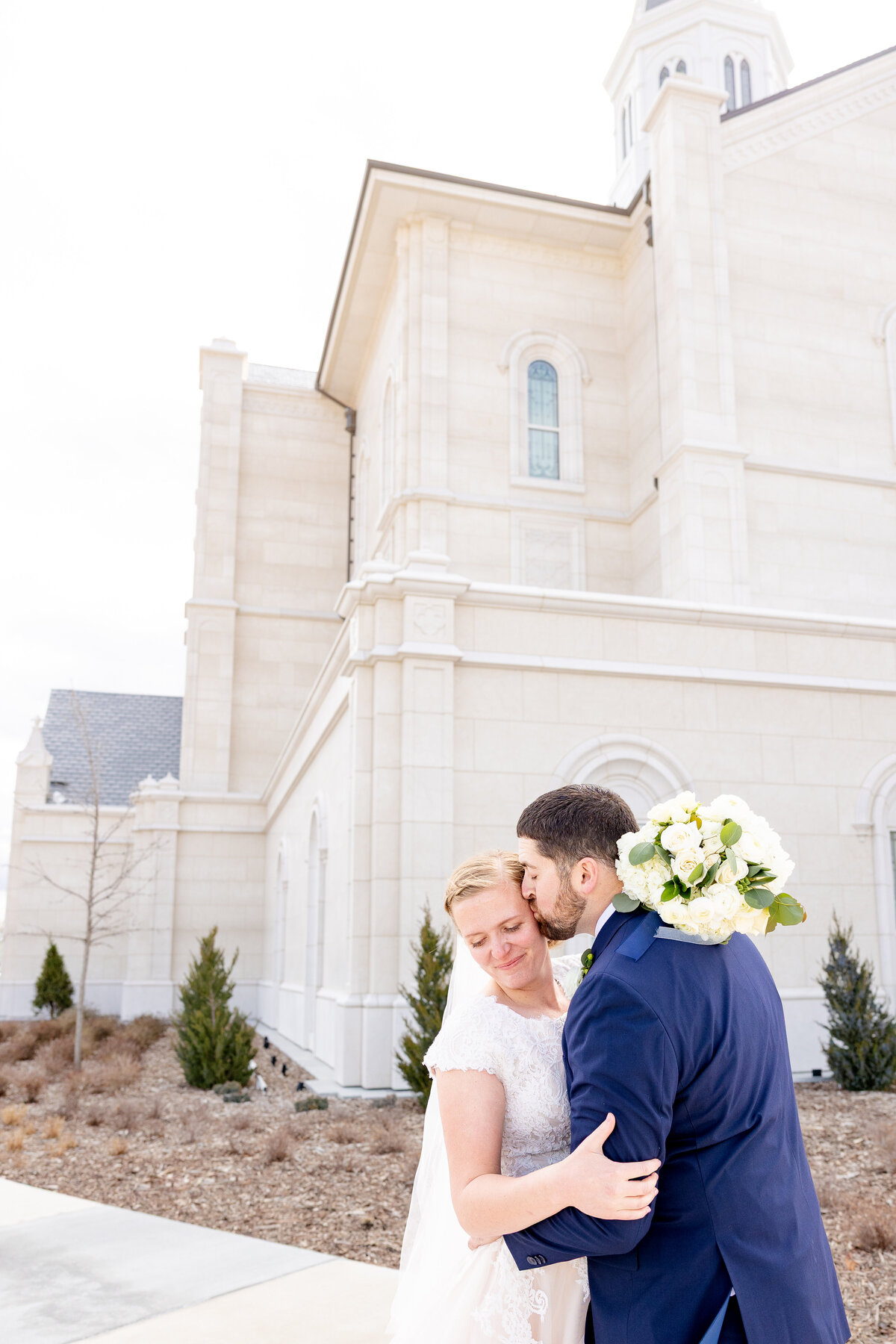  Groom gently kisses his bride on the forehead outside the Taylorsville Utah Temple on their wedding day.