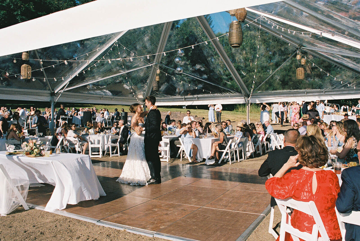 A bride and groom dance at an outdoor wedding reception.