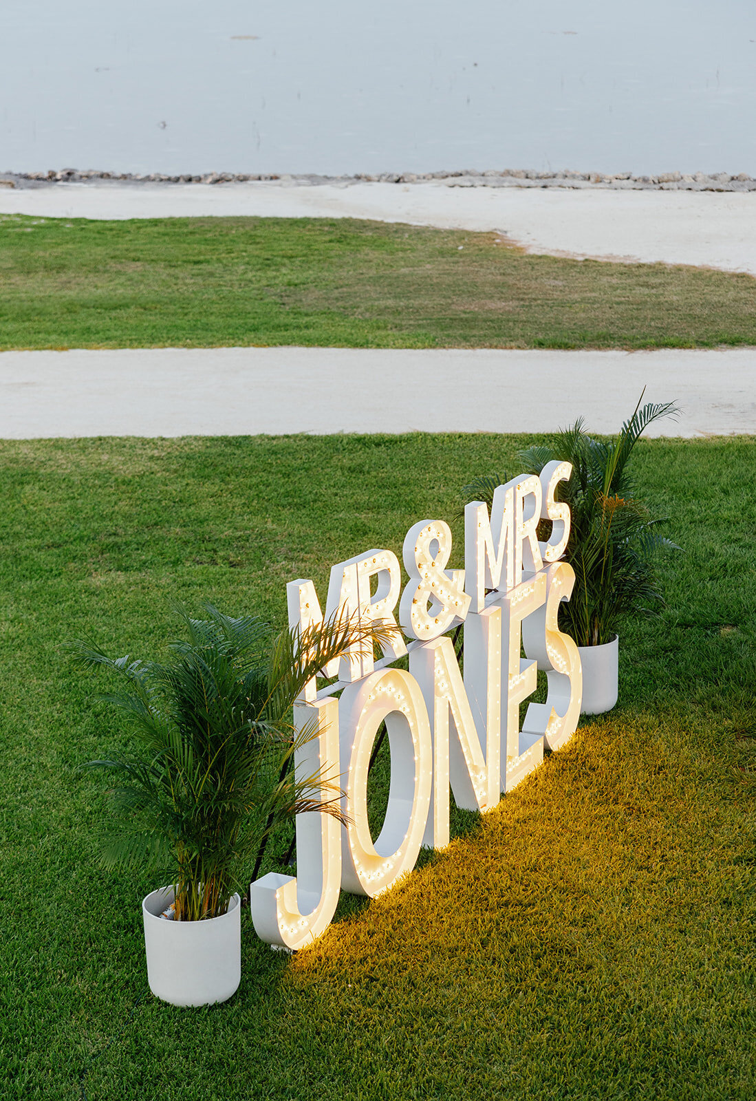 A stunning outdoor wedding reception featuring a personalized "Mr. & Mrs. Jones" illuminated sign on the lush green lawn at Table Key, Islamorada. Photography by Claudia Amalia Wedding Photography.