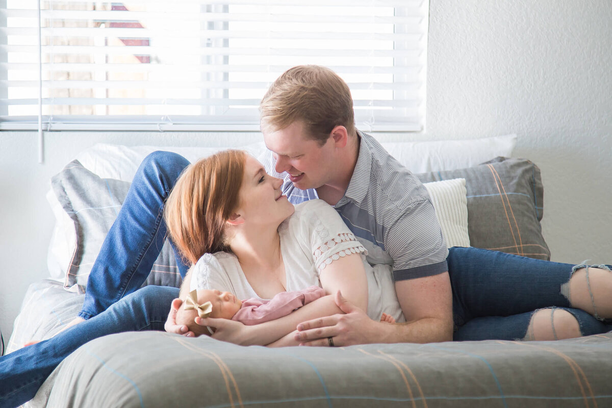 Couple lovingly looking at each other on a bed with their newborn baby girl