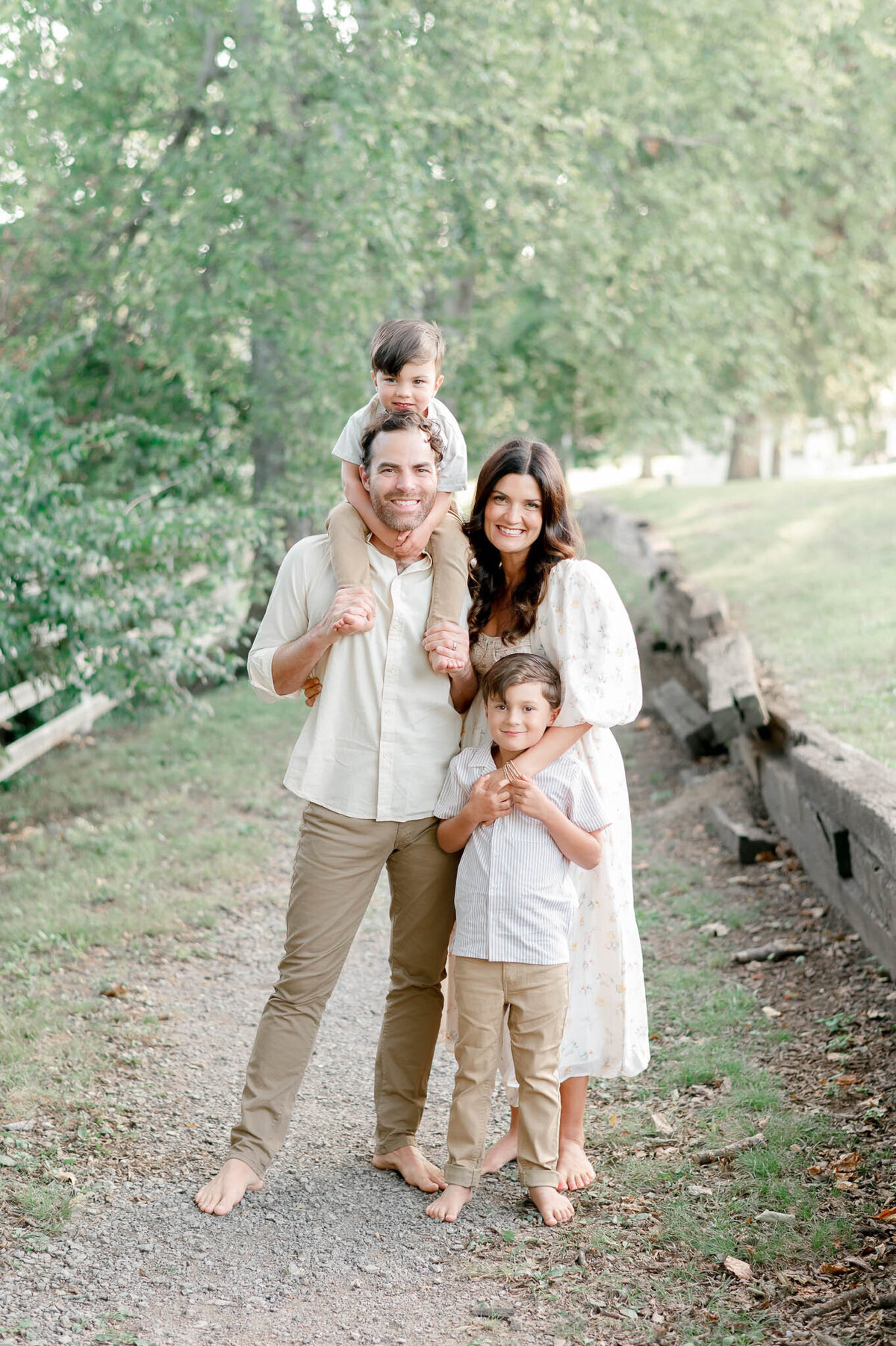 Family of 4 smiles at a little boy sitting on dad's shoulders