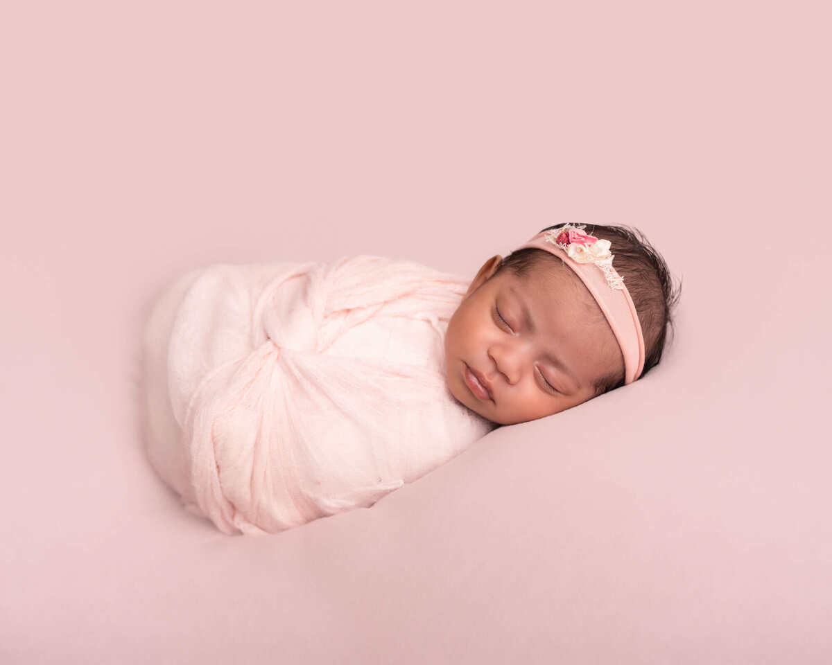 A newborn baby girl snoozes while wrapped in a pink blanket