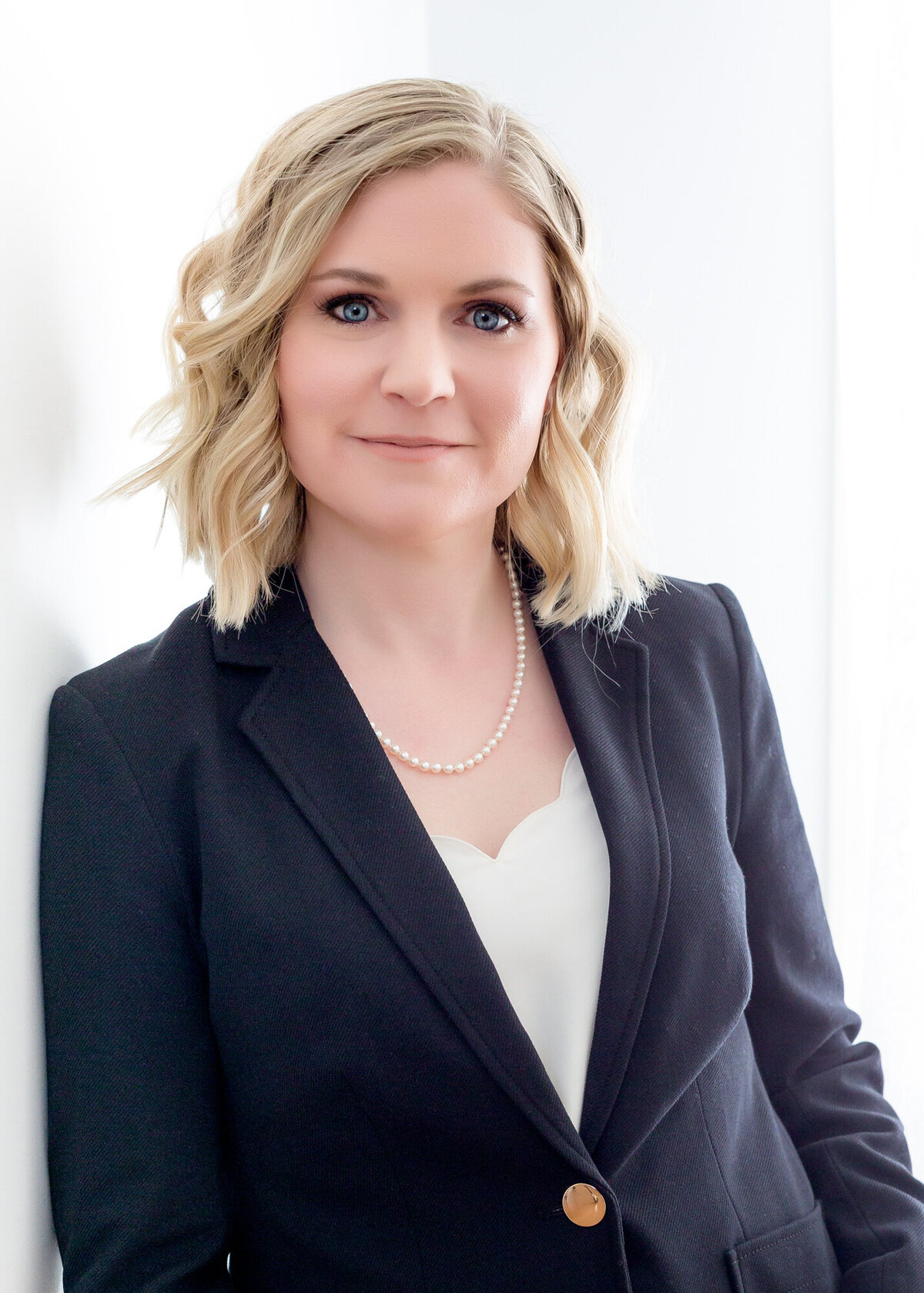 Female headshot client wearing a black suit leaning against a wall