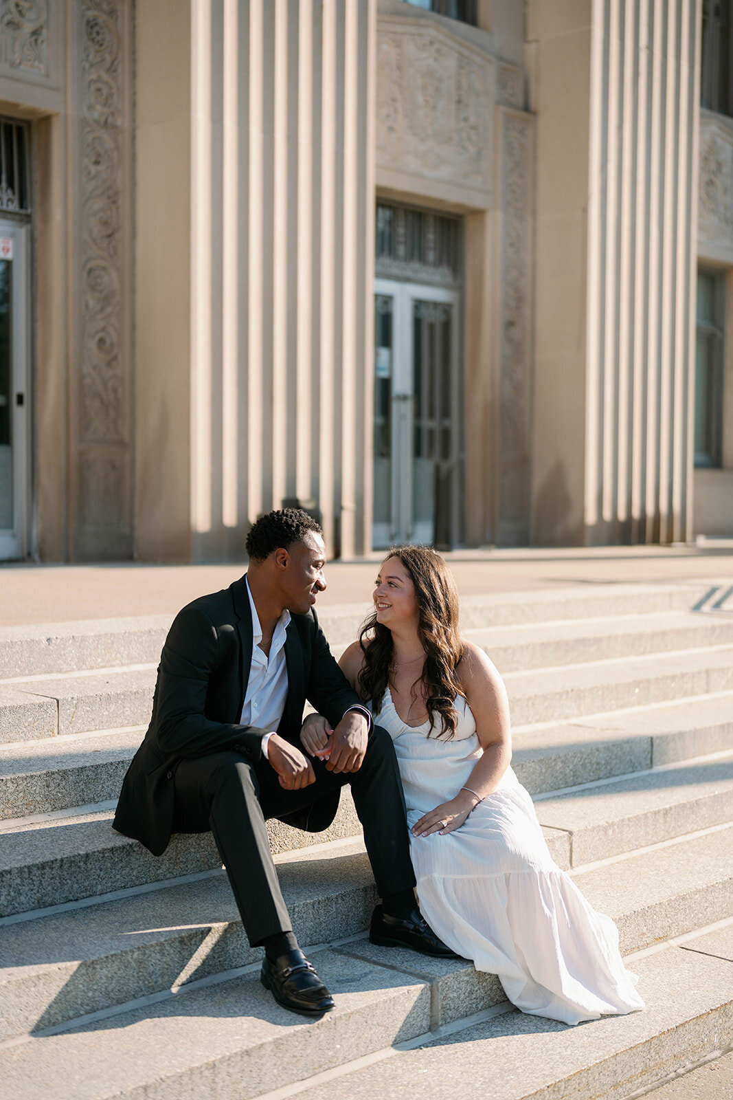 Bright and airy engagement photo of couple sitting together outside historic Kalamazoo building.
