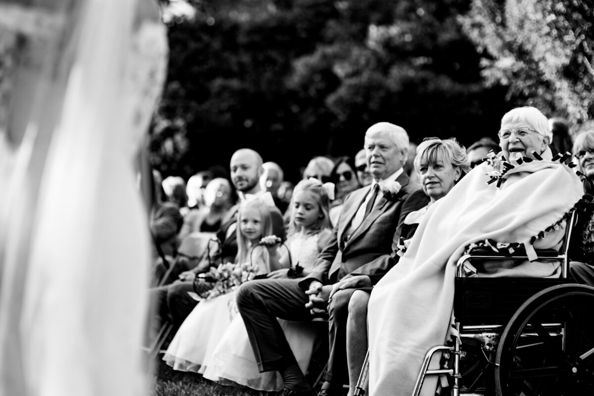 One of the top wedding photos of 2020. Taken by Adore Wedding Photography- Toledo, Ohio Wedding Photographers. This photo is of a grandma smiling and watching her grandson get married at the Toledo Zoo Gardens