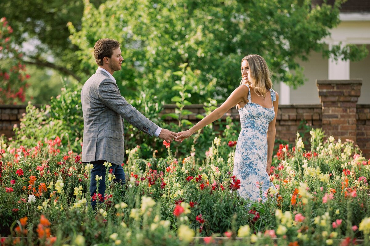 engaged couple walk hand in hand through garden