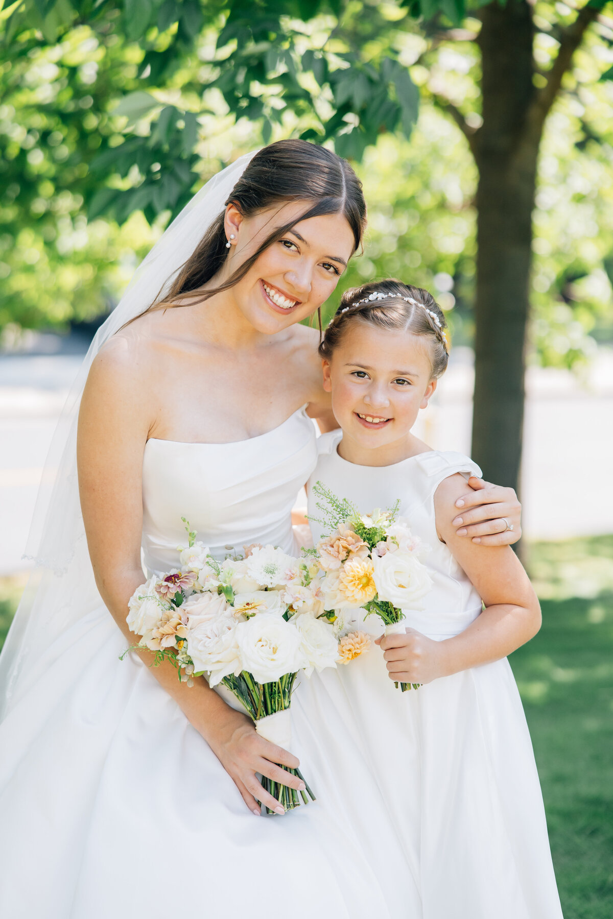 Bride hugging her flower girl in white satin dresses holding blush and tan flowers
