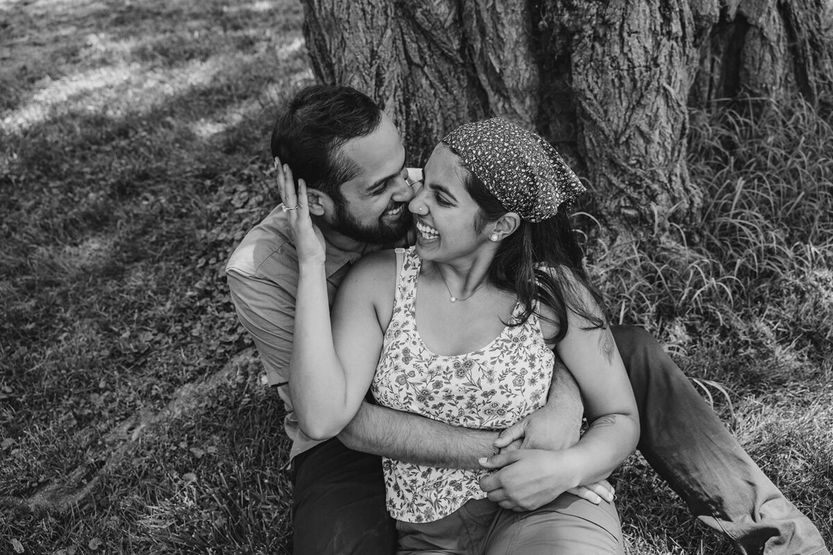 A couple sitting down and leaning on each other against a tree 