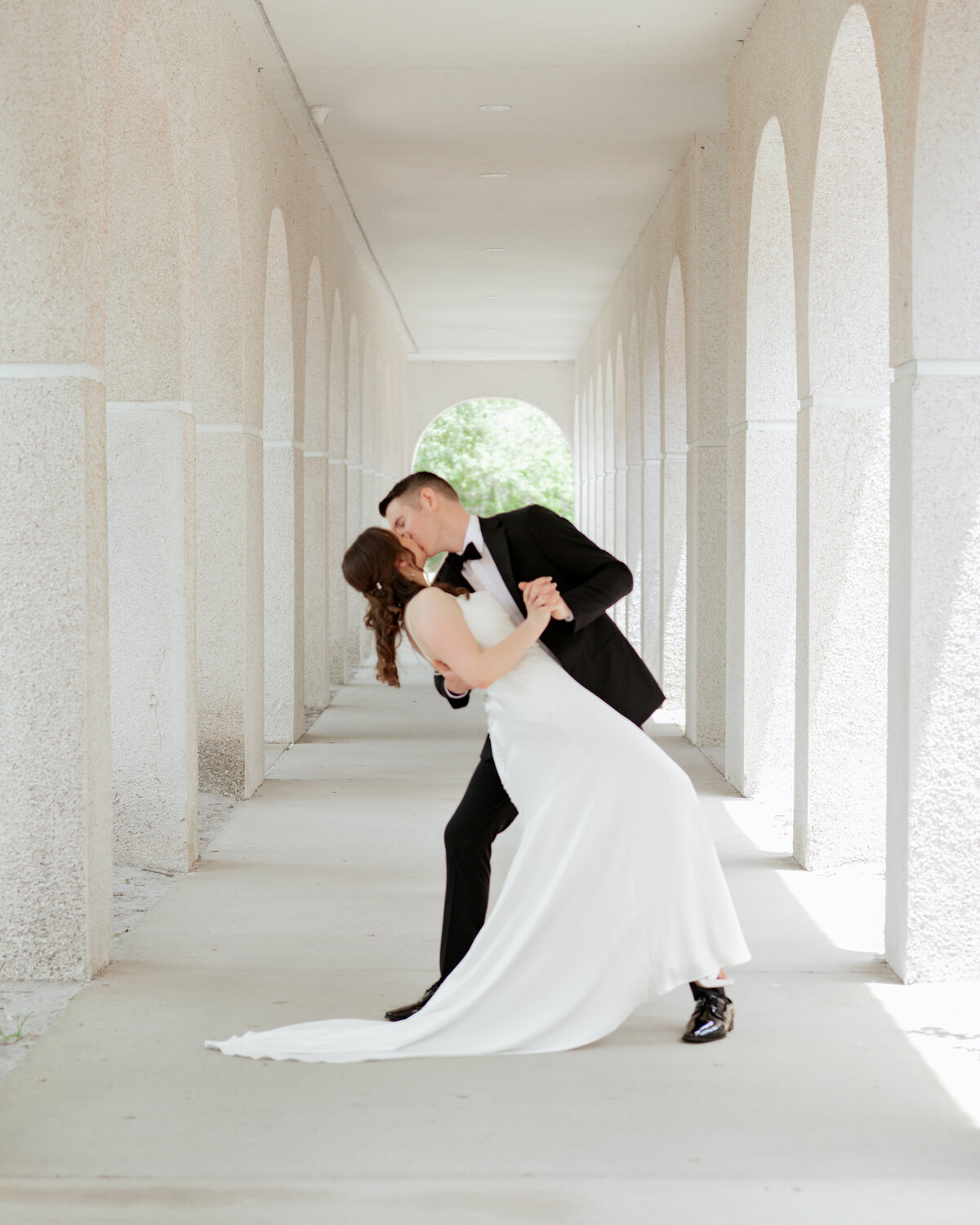 a catholic bride and groom share a dip kiss outside a mission style catholic church in st. augustine florida ahead of their catholic wedding mass