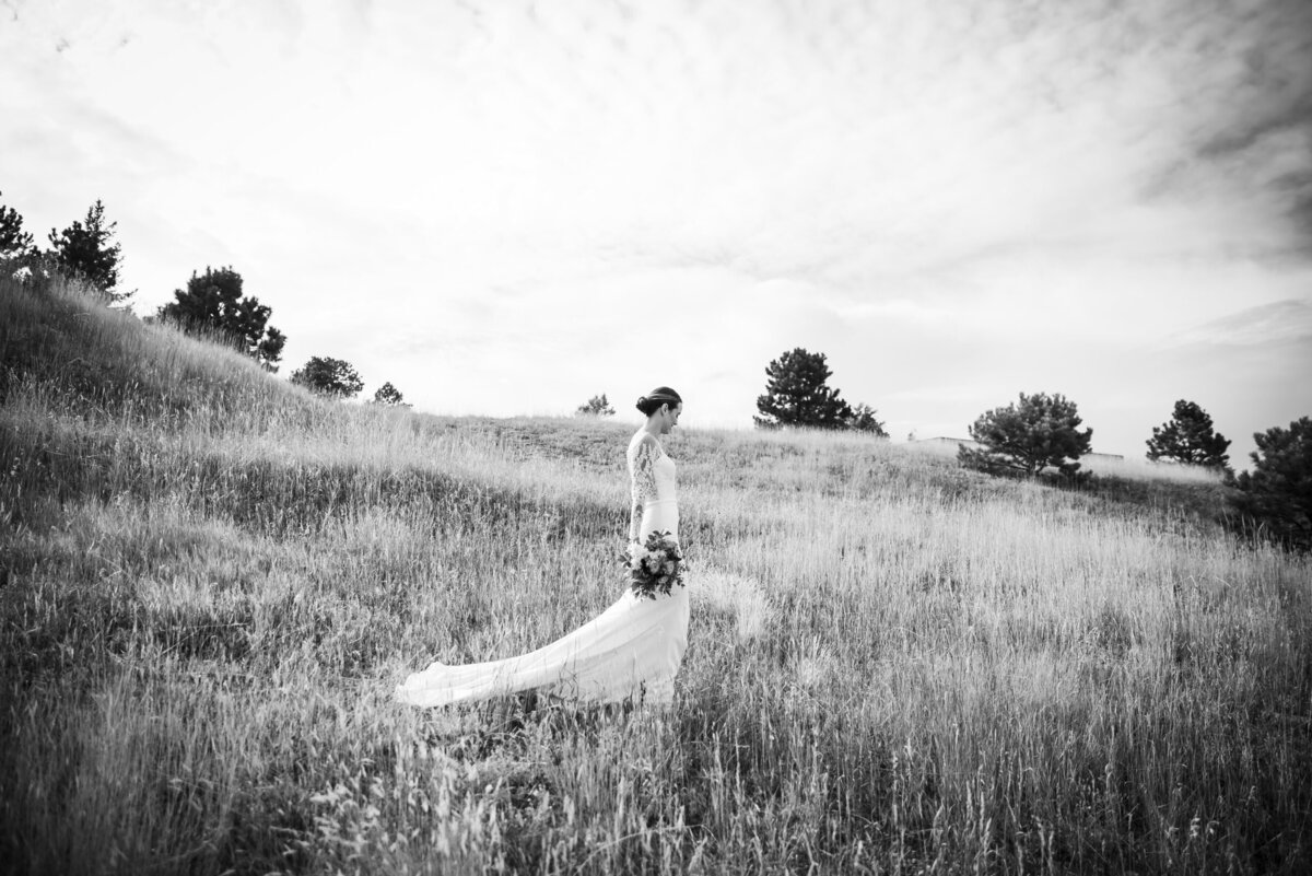 A wide angle shot of a bride walking through a field holding her bouquet.