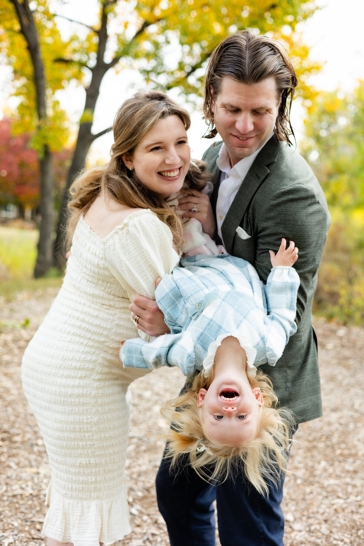 Mom and dad hold their toddler daughter between them and tip her upside down as she laughs.