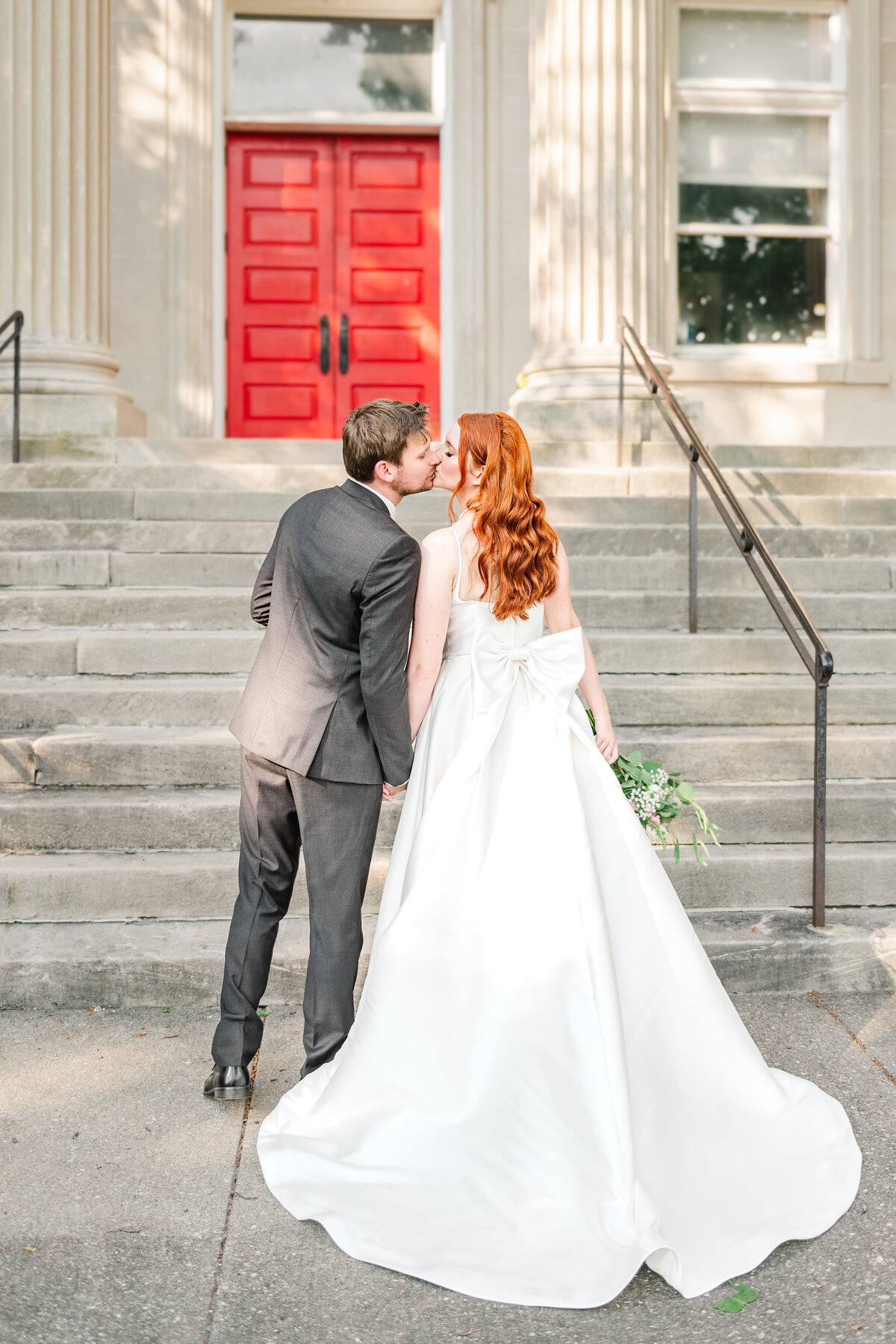 bride and groom kissing and showing bow on back of wedding dress