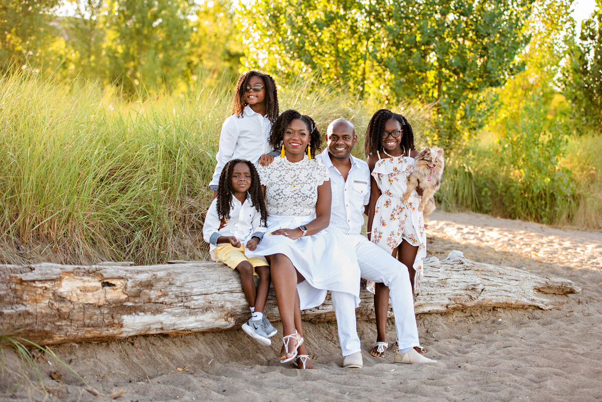 Black family sitting on a log at the beach with their dog for their Burlington beach family photography session