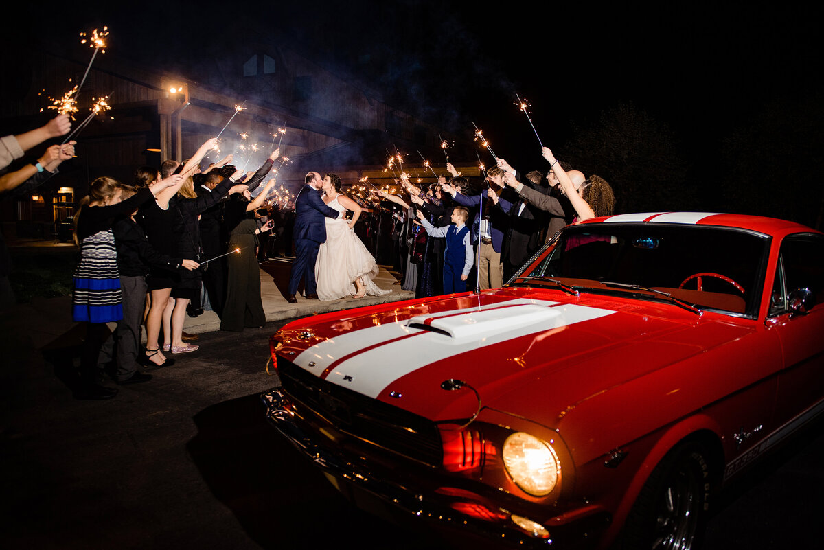 Bride and Groom sharing a kiss as they head to their vintage car and their guests hold sparklers for the exit