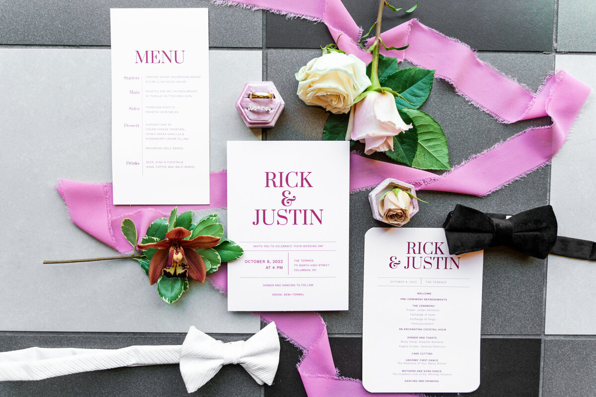 Flat-lay of a wedding invitation, menu, program, florals, rings, and bow ties at The Graduate Hotel in Columbus, Ohio.