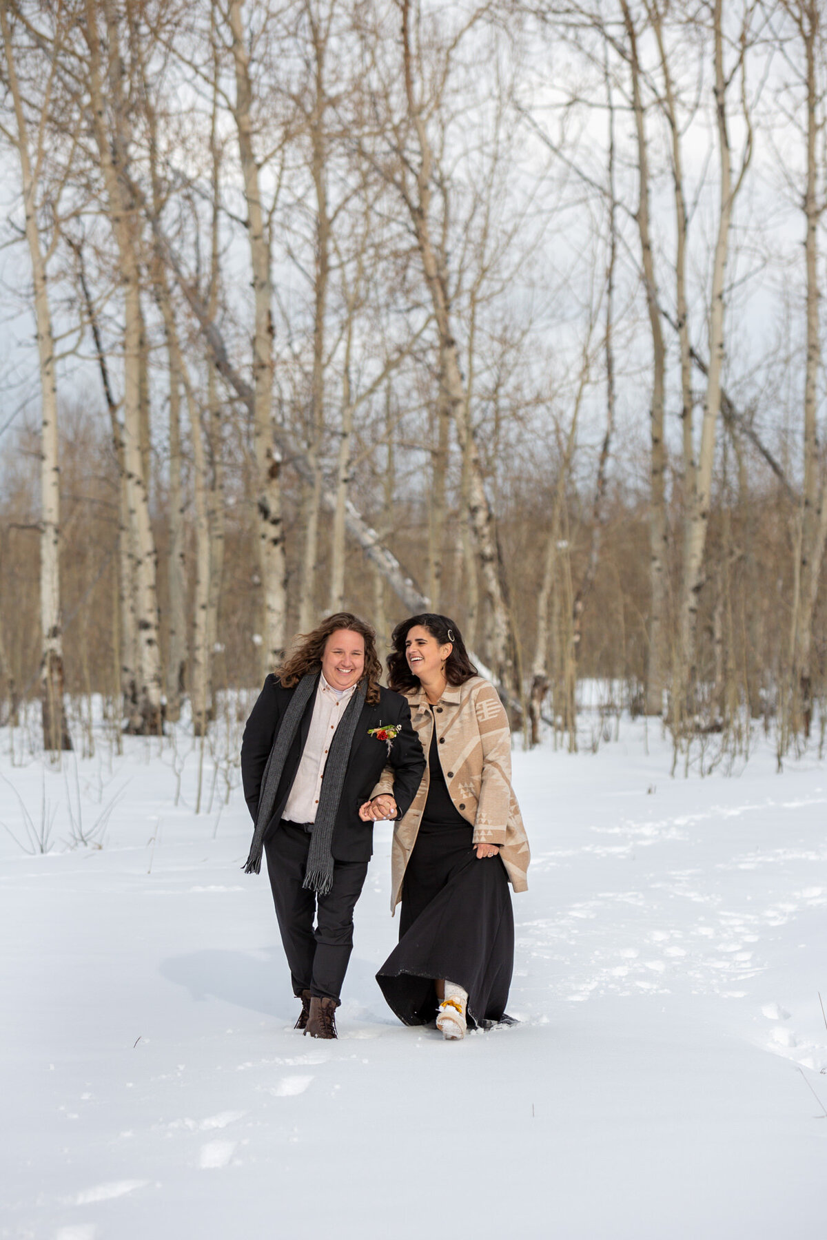 Two brides walk side by side through the snow on their Wyoming elopement day.