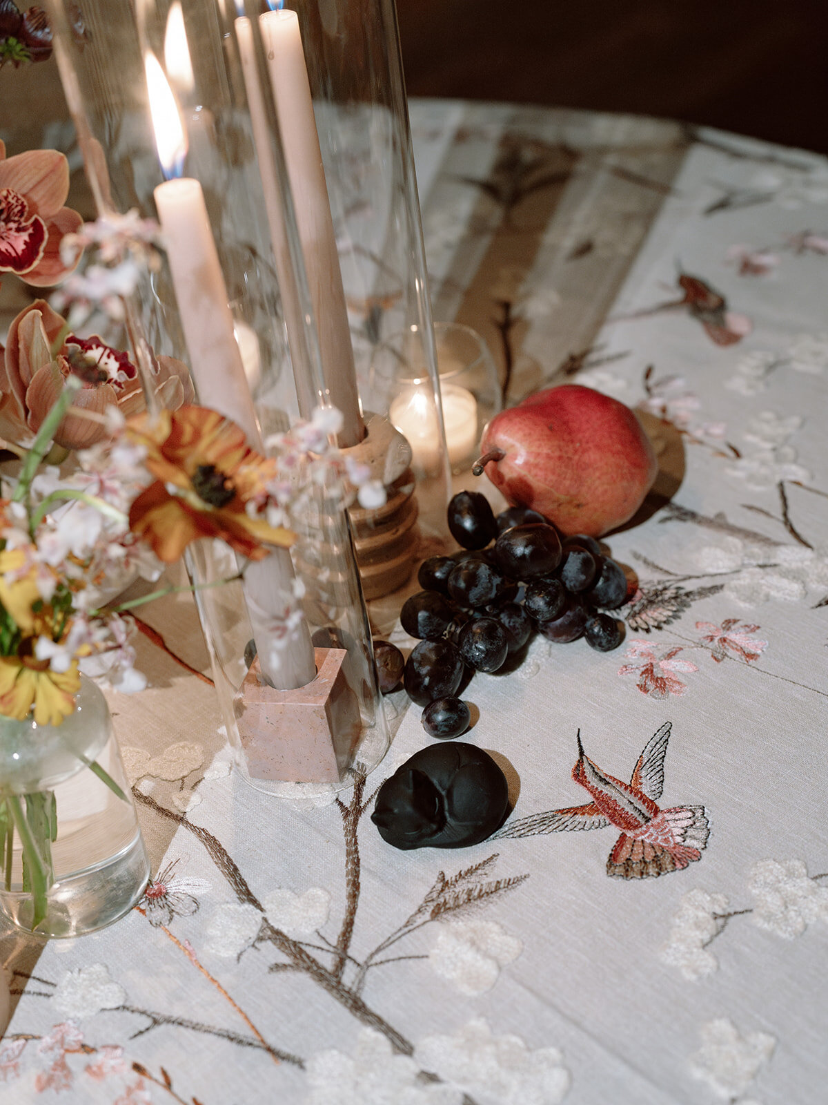 Clustered and styled floral arrangements, fruits, and art pieces for fall wedding reception. Low centerpieces mixed with ikebana arrangements and bud vases decorate the reception tables at this fall wedding. Floral centerpieces featuring orchids, ranunculus, sweet peas, and bittersweet. Styled wedding tables with fruits, curated candles, and floral arrangements. Tasteful fall color palette of copper, ruby, gold, burgundy, rust, and lavender. Design by Rosemary & Finch Floral Design in Nashville, TN.