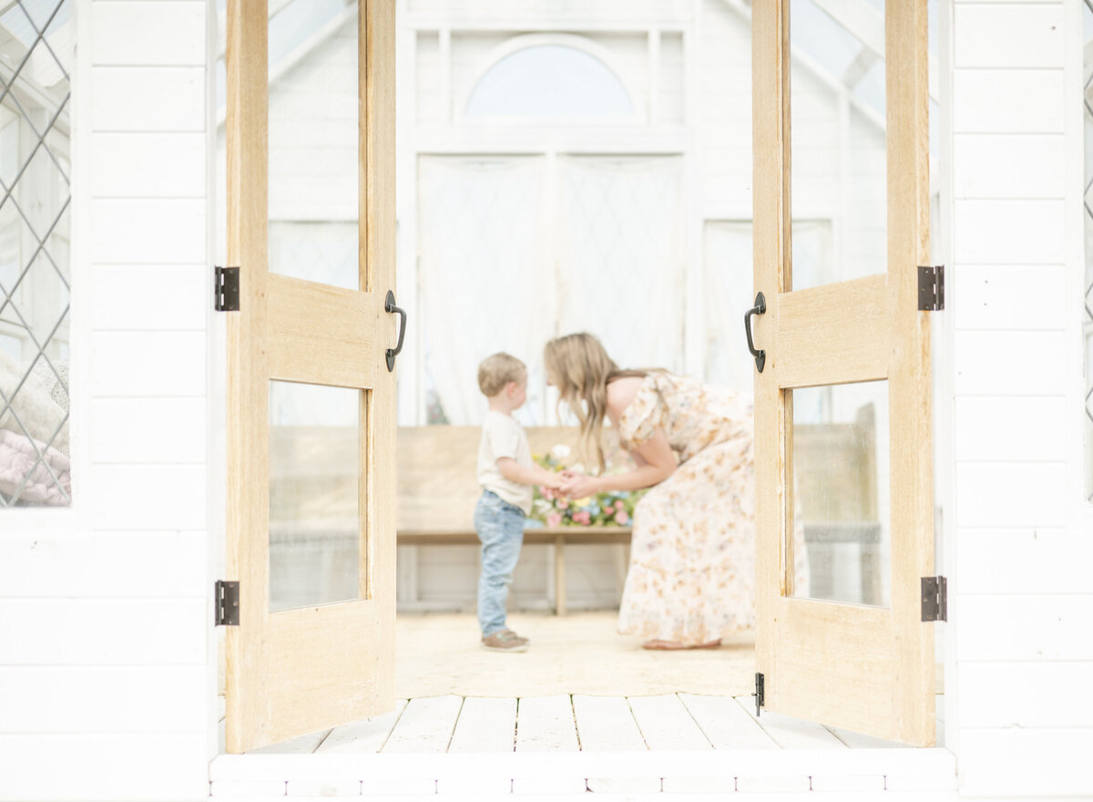 Mom and toddler playing together inside a sunroom with soft natural light and wooden walls.