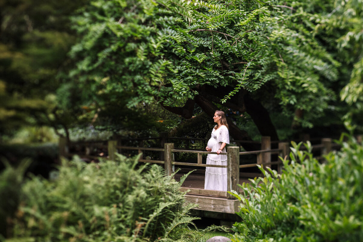 pregnant woman in white dress standing among greenery on platform in san francisco botanical gardens