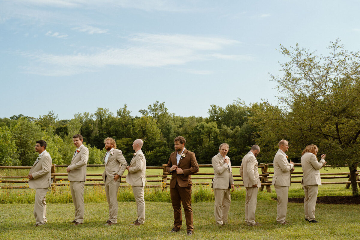 Groom standing confidently with groomsmen lined up behind him outdoors