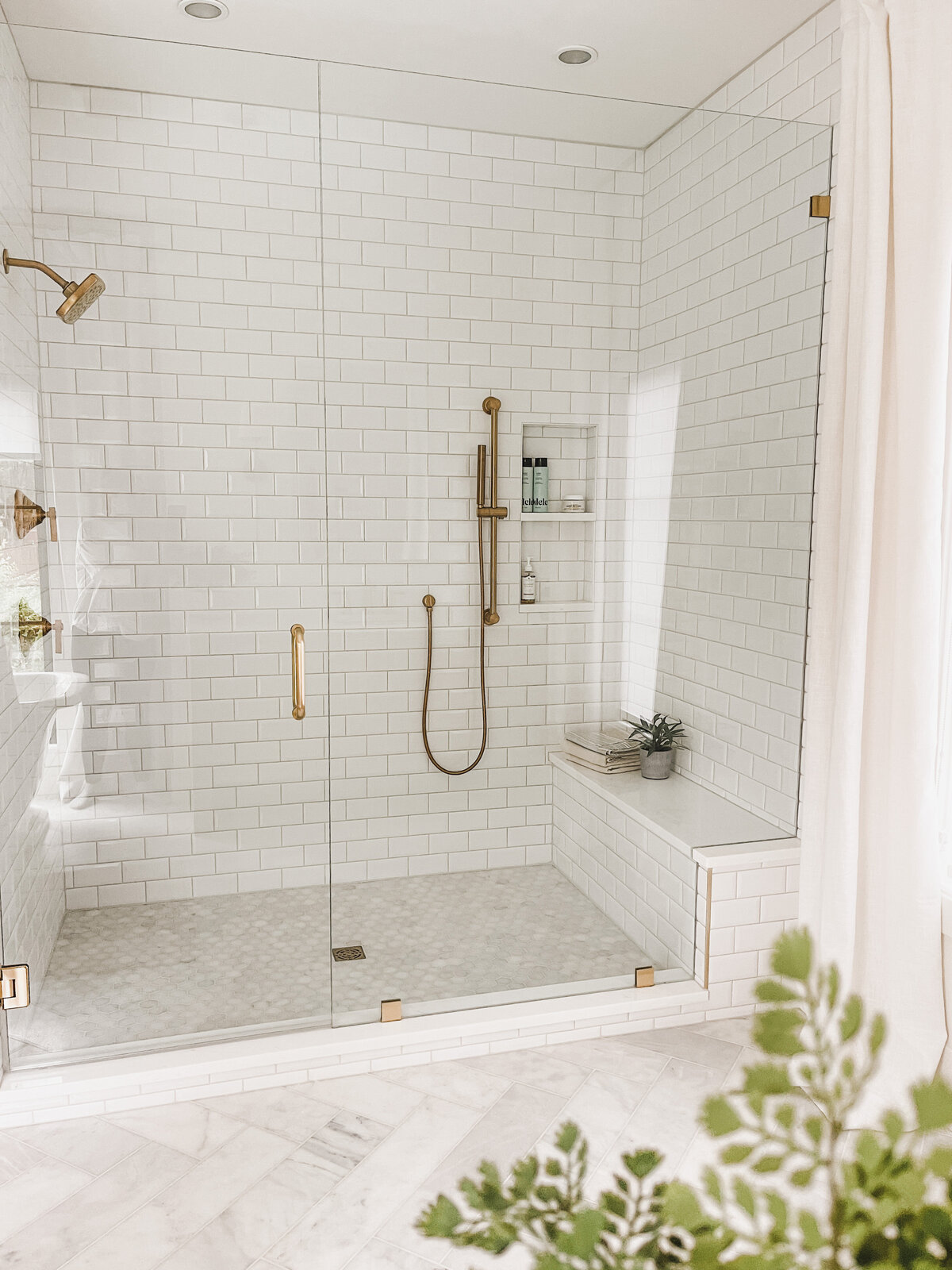 The walk-in shower in the primary bath features a marble floor and custom seating bench with brass fixtures
