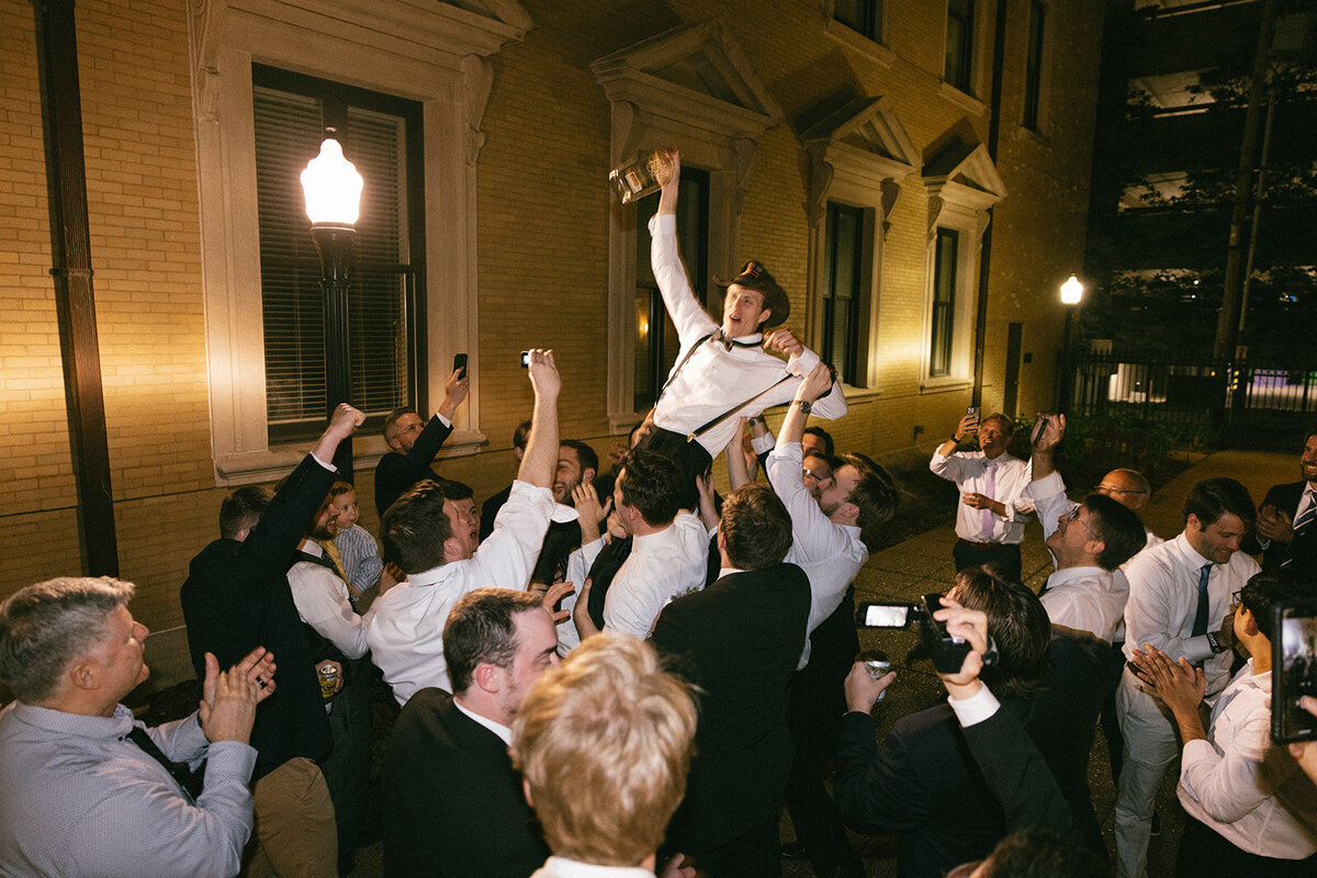Groomsmen lift up groom wearing a cowboy hat in joyful celebration after a wonderful wedding in Nashville, TN.