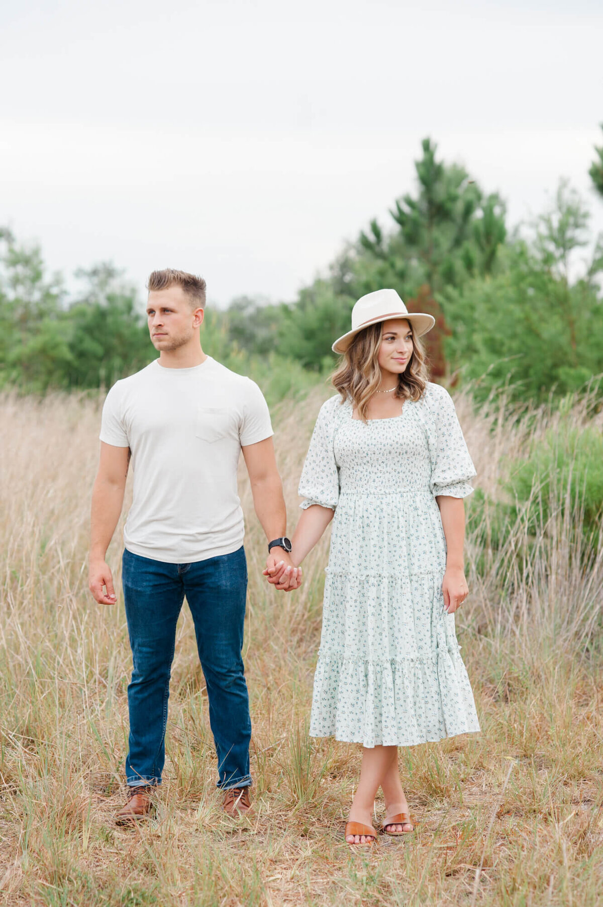 Parents dressed stylishly standing in a field holding hands looking in the opposite direction