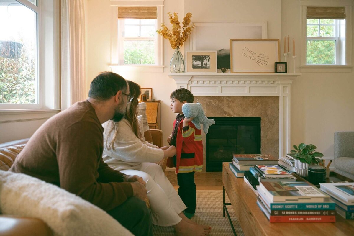 boy wearing fireman jacket with stuffed whale at home with family