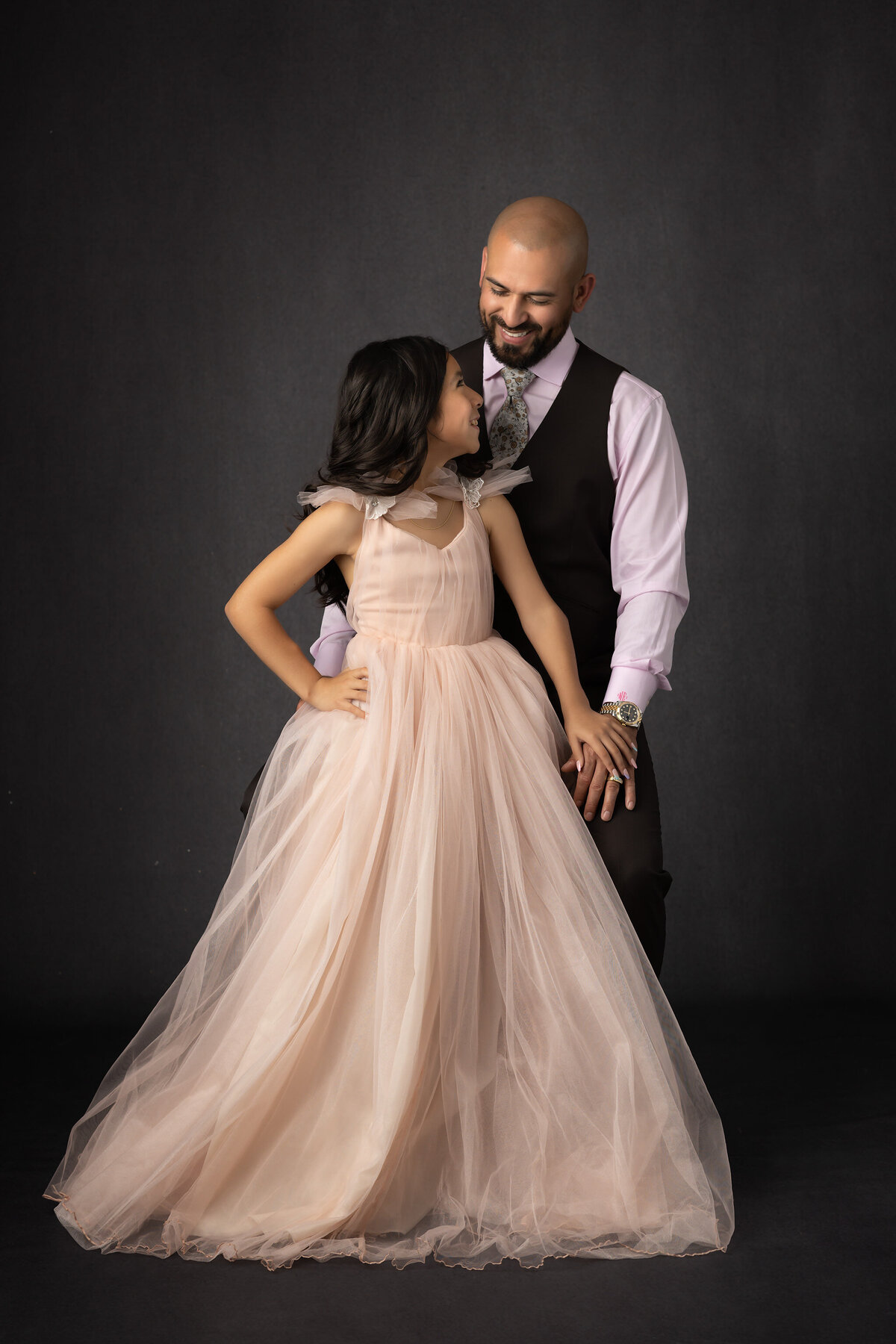 A Dallas family photographer captures a father and daughter sharing a joyful moment, with the daughter in a soft pink dress and her father dressed in a suit.