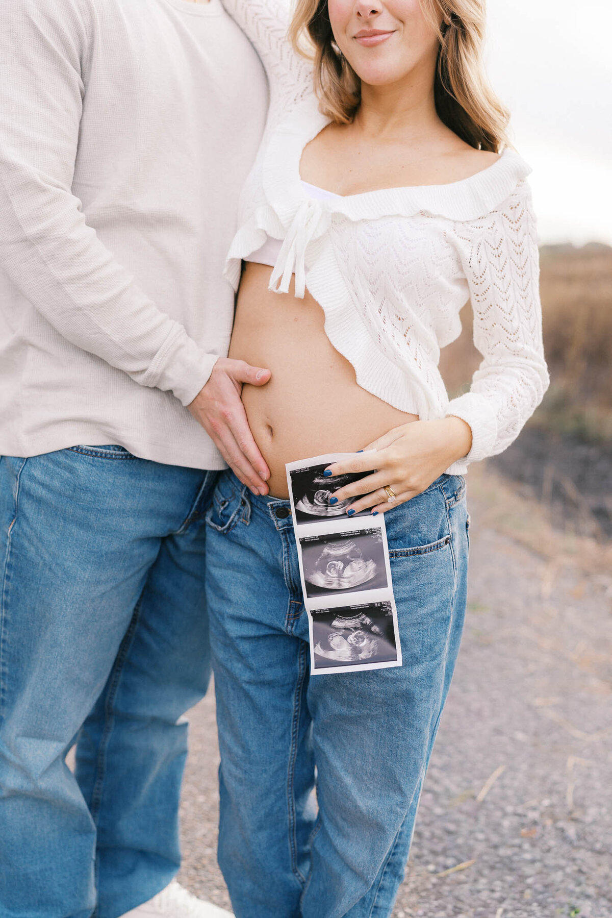 man holds pregnant wife's belly and holds ultrasound during golden hour in knoxville tennessee