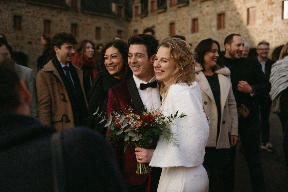 Mariés entourés de leurs proches, sourires et bonheur partagés devant le château de la Rouerie. Photo Kamescop, vidéaste et photographe mariage en Bretagne.