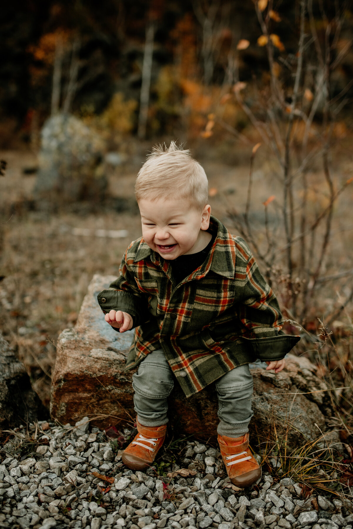 A toddler boy dressed in a flannel, boots, and jeans giggles during Fall Family Pictures in Duluth, Minnesota.