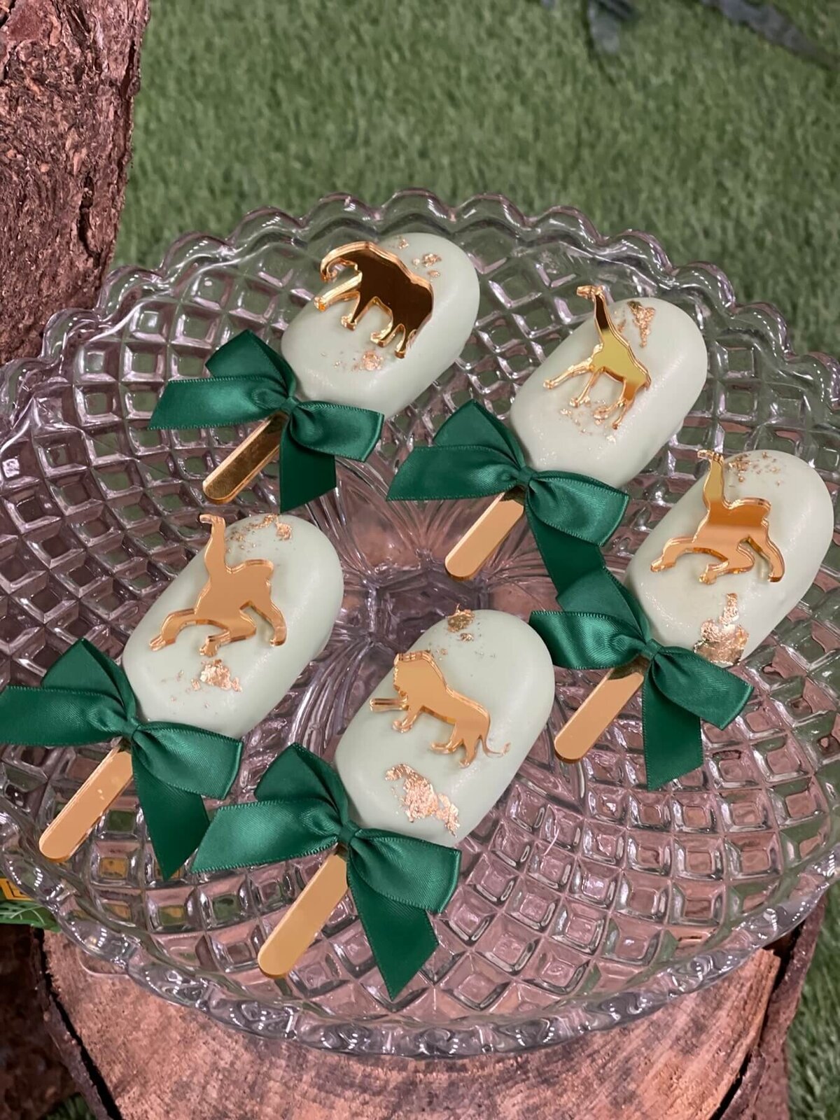 Pretty white cake pops with gold animal decoration and a green bow sitting on a glass plate