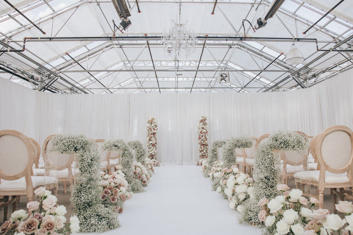 Luxurious indoor wedding ceremony with roses and baby's breath lining the aisle