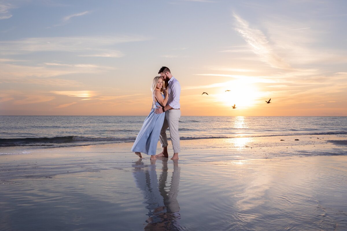 A wide angle shot of a stunning couple with the sunset, ocean and birds captured by Love and Style Photography at Siesta Key Beach during an engagement session