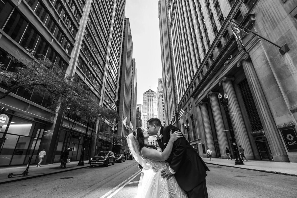 A black and white photo of a bride and groom kissing on a city street.