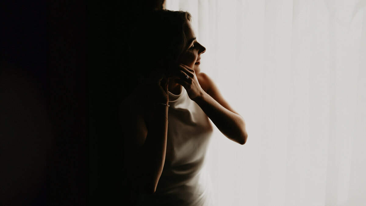 A bride puts her earring in whilst looking out the window at The Need in London.