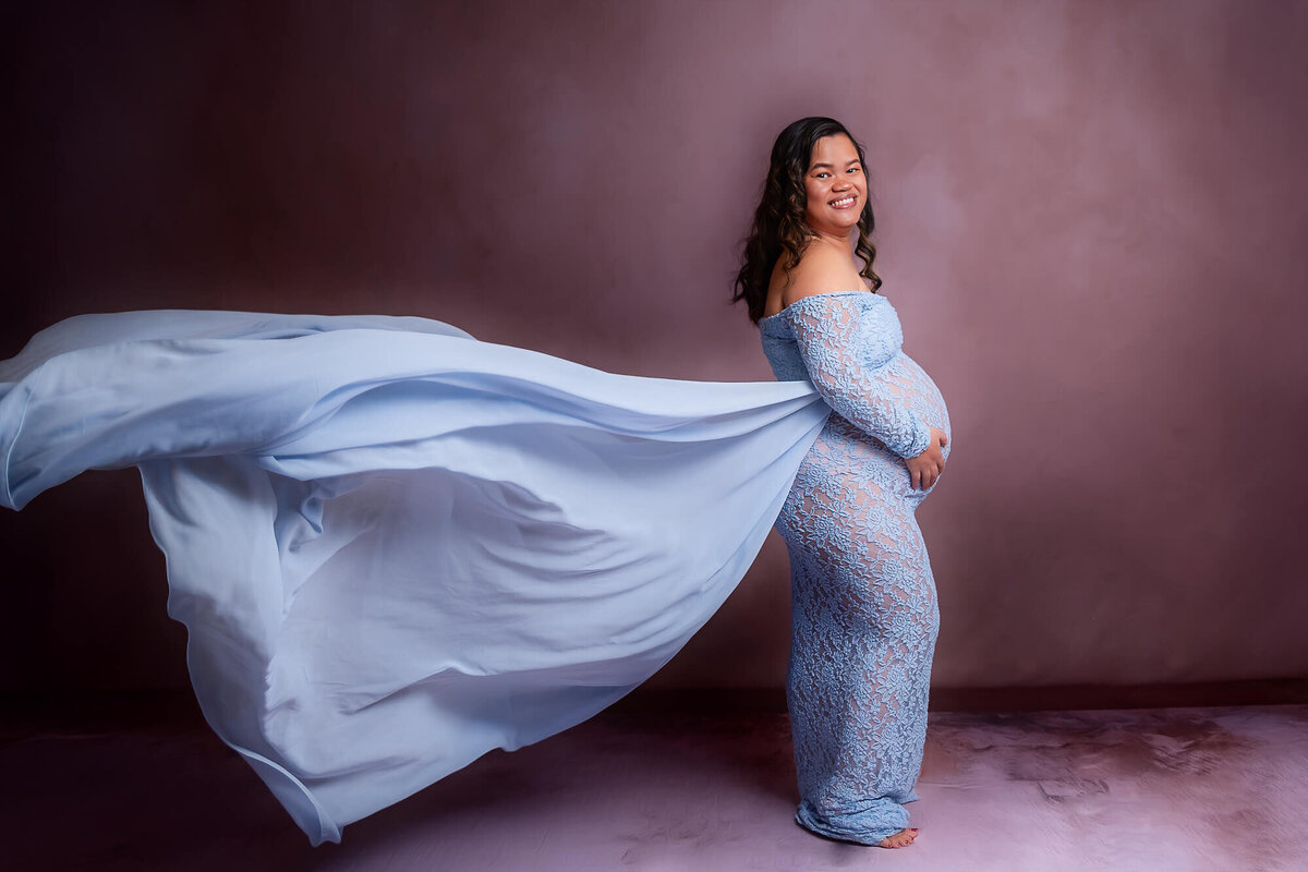 A pregnant woman in a blue dress smiles and poses for a photo, showcasing her beautiful baby bump at  studio in Cleveland, Ohio