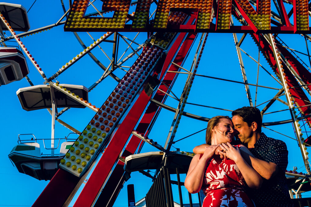 A man and woman hugging under a ferris wheel.