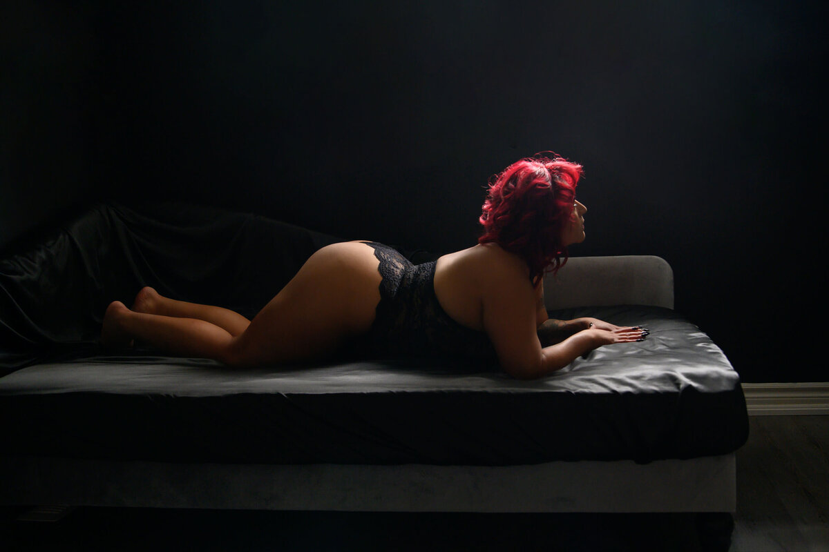 Woman on her belly wearing black bodysuit for her Toronto luxury boudoir photos