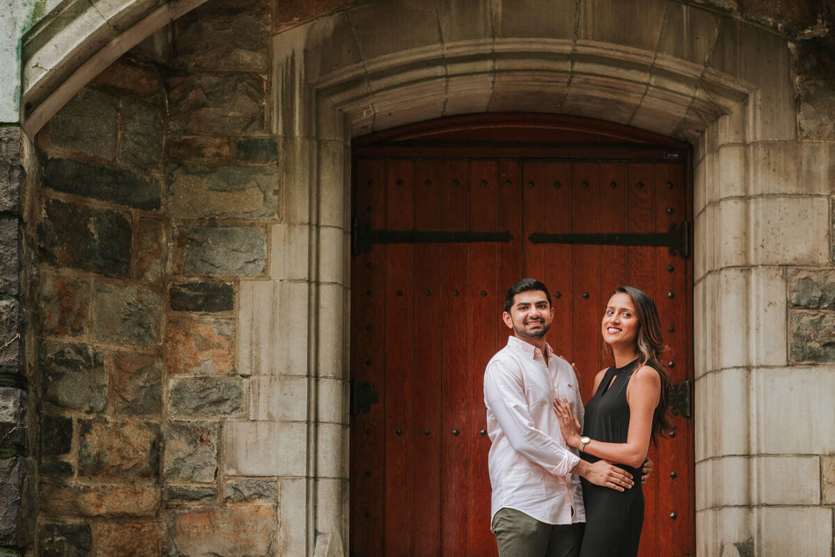 A couple poses in front of a grand wooden door with stone archways during their Lehigh Valley engagement session.