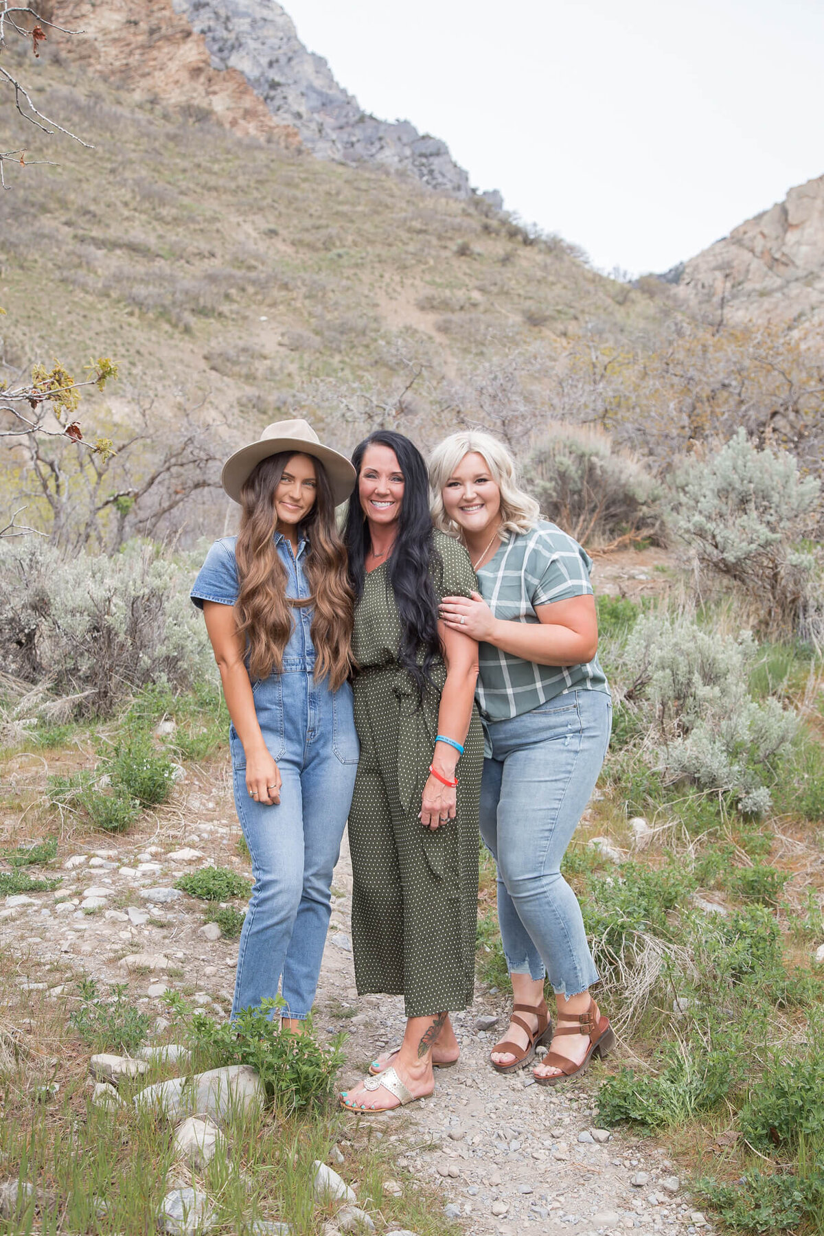 three smiling women in blue and green on mountain trail