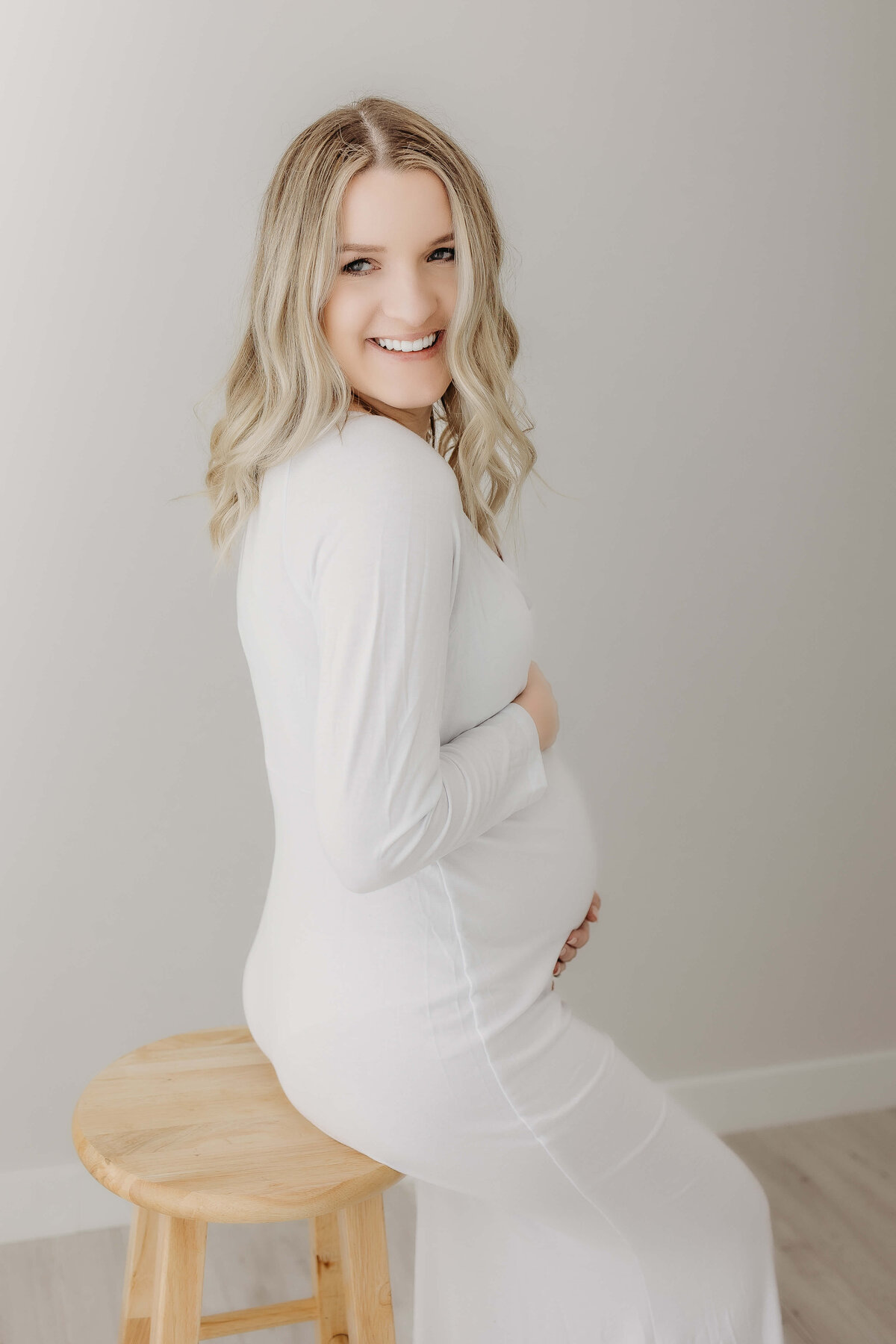 expecting mom in white dress sitting on stool laughing maternity picture luci levon photography eau claire wi