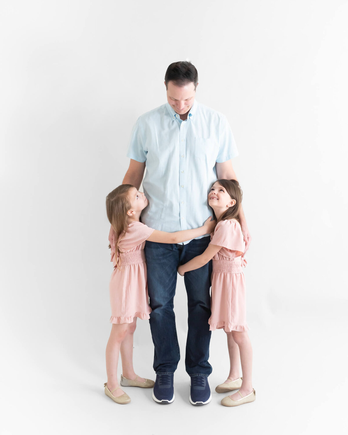 dad and daughters emracing in studio session on a white background