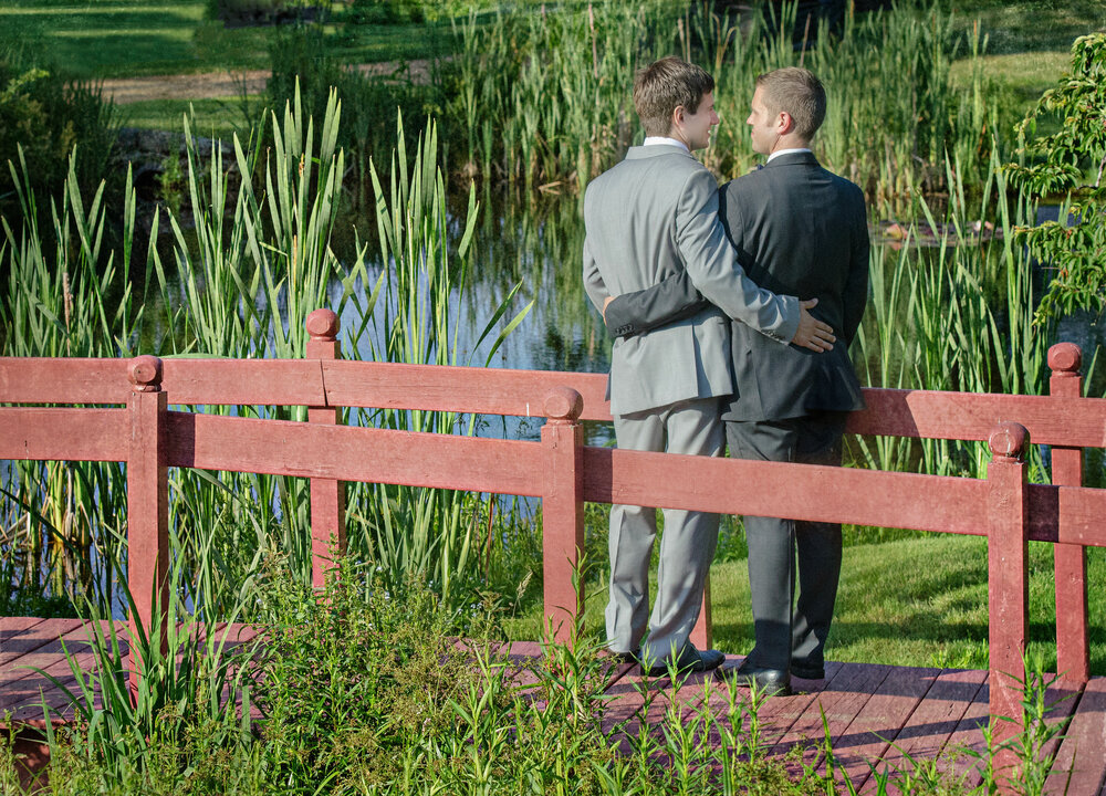 Two grooms embracing on a small bridge