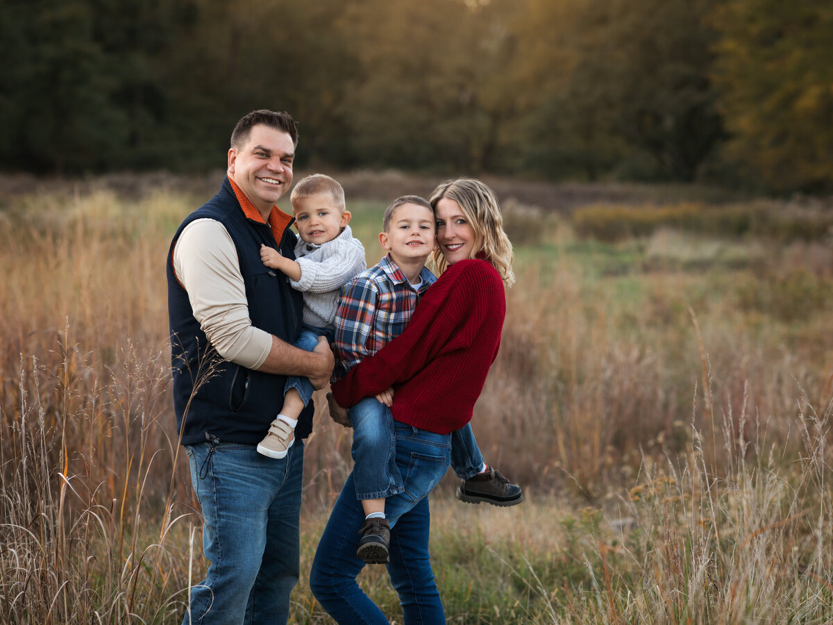 mom dad and two sons posed in field for family photoshoot 