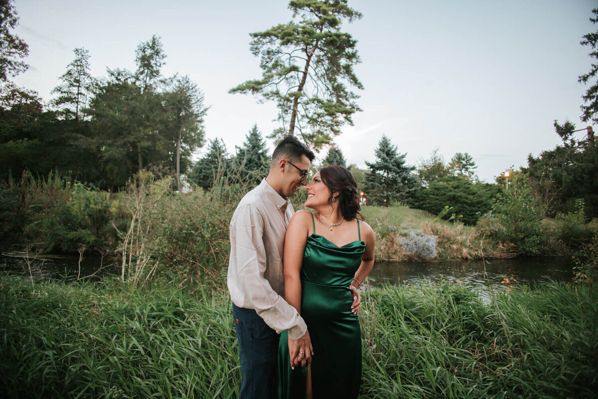 The bride and groom-to-be share a joyful moment by the water during their Lehigh Valley engagement session at Rosewood Garden. 