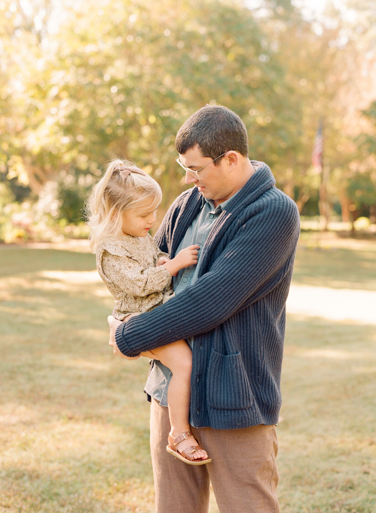 Dad holds daughter during a fall family portrait session in Raleigh. Family walking during their family portrait session in Wake Forest, NC. Photographed by Raleigh family photographer A.J. Dunlap Photography.